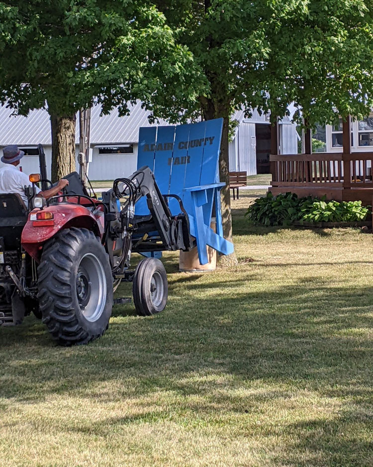 A small tractor setting up the very large blue 'Adair County Fair' chair.